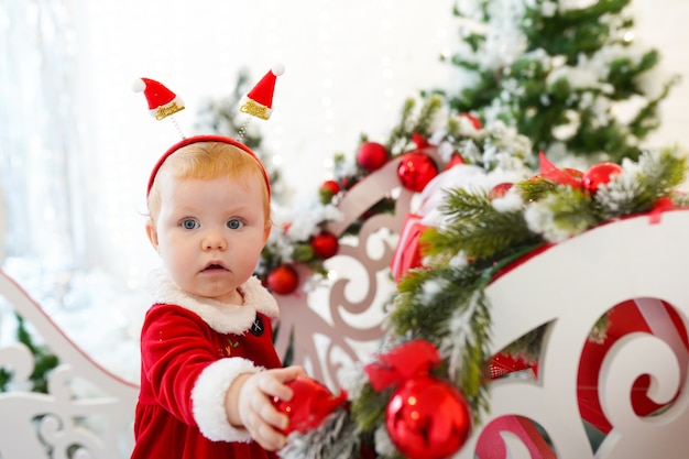 Little girl with red hair and blue eyes in Santa's red dress playing Christmas toys