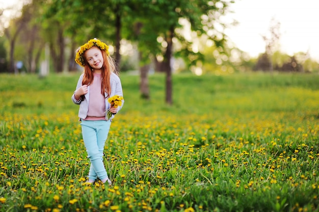 A little girl with red hair smiles against a field of dandelions and green grass. Summer, childhood, holidays. space for text, copy space