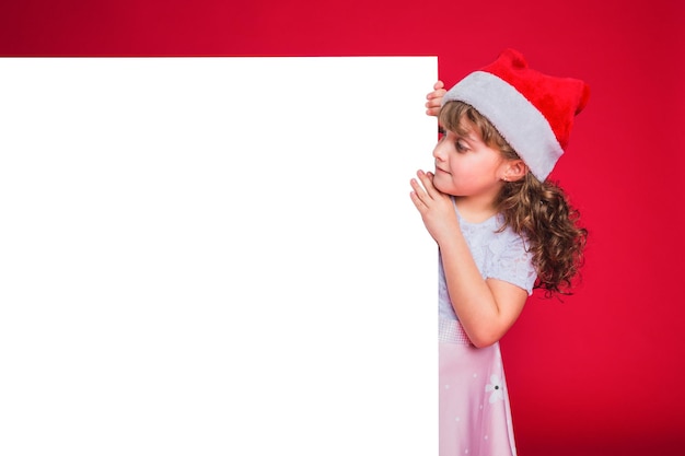 Photo little girl with red santa claus hat holding a billboard.