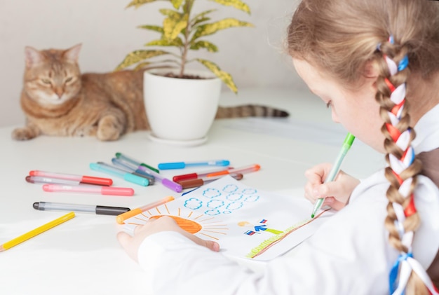 A little girl with ribbons in her hair draws at a table