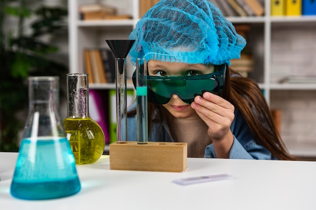 Foto bambina con occhiali di sicurezza e retina per capelli facendo esperimenti scientifici