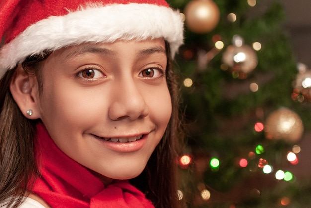 サンタクロースの帽子とクリスマスの装飾の背景を持つ少女