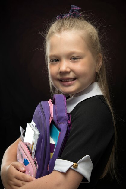 Little girl with a school backpack in her hands on a black wall. Back to school and education concept