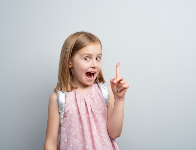 Little girl with school backpack pointing finger up