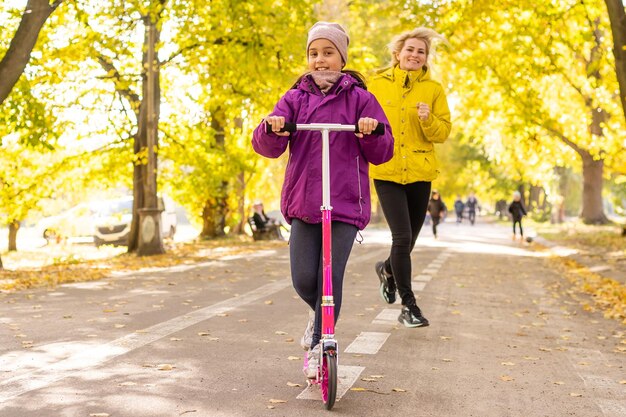 Bambina con uno scooter nel parco autunnale alla soleggiata giornata autunnale