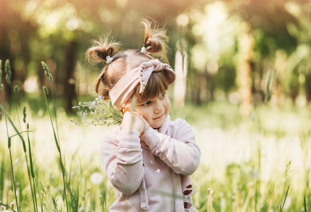 A little girl with a small bouquet of flowers in the park in the summer. Cute portrait