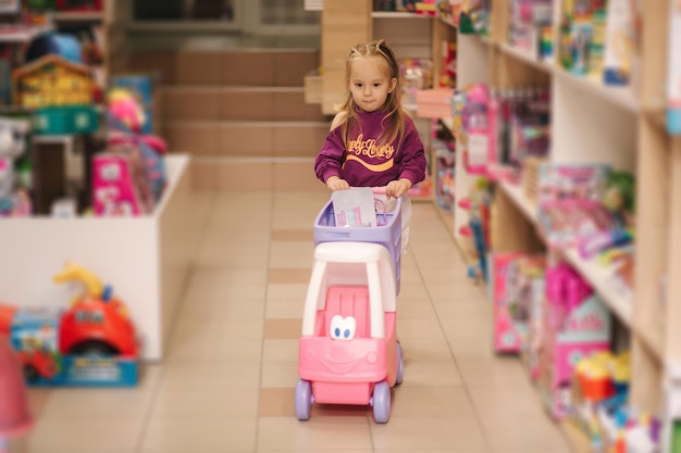 Little girl with small shopping cart in kids mall happy girl choosing what to buy in toy store