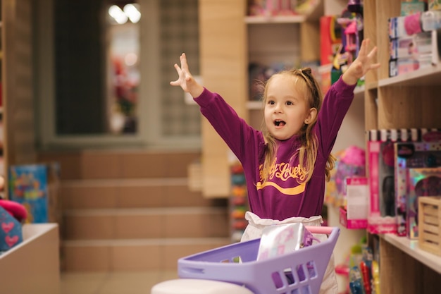 Little girl with small shopping cart in kids mall happy girl choosing what to buy in toy store