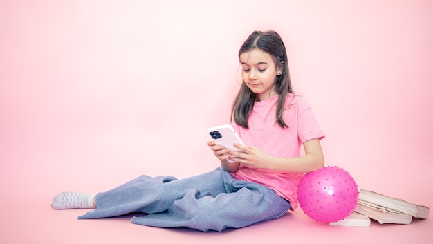 Little girl with a smartphone in her hands on a pink background copy space