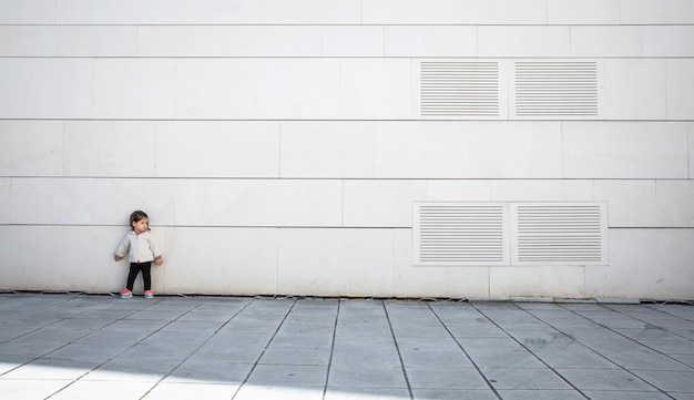 Little girl with sportive look posing in front of a modern white stone wall