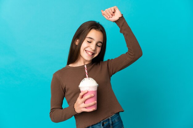 Little girl with strawberry milkshake isolated on blue background celebrating a victory