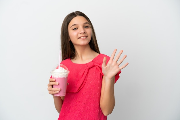 Little girl with strawberry milkshake over isolated white surface saluting with hand with happy expression