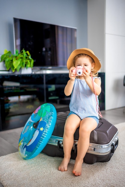 Little girl with suitcase baggage luggage and inflatable life buoy playing with toy camera and ready to go for traveling on vacation