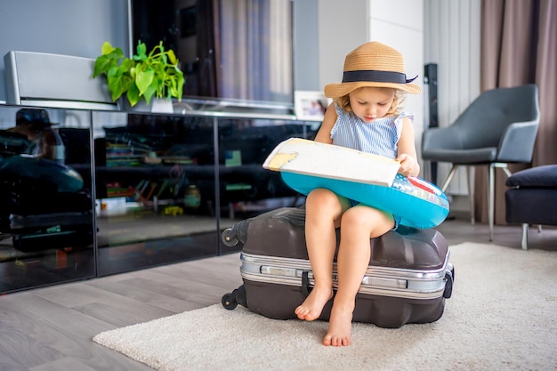 Little girl with suitcase baggage luggage and inflatable life buoy reading map and ready to go for traveling on vacation