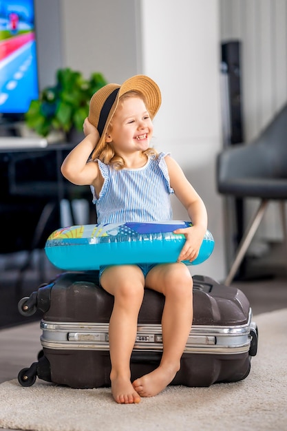 Little girl with suitcase baggage luggage and inflatable life buoy ready to go for traveling on vaca