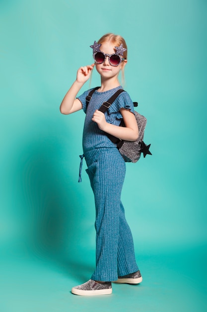 Little girl with a tail in stylish clothes and sunglasses on blue background