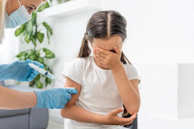 A little girl with tears in her eyes is very afraid of vaccination. The baby cries closing his eyes in pain. Portrait of a sobbing child who is injected in the shoulder. Children's medical concept,