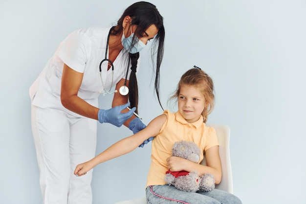 患者に予防接種をしている制服を着たテディベアの医者を持つ少女