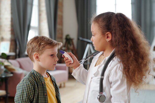 Little girl with thermometer measuring body temperature of boy