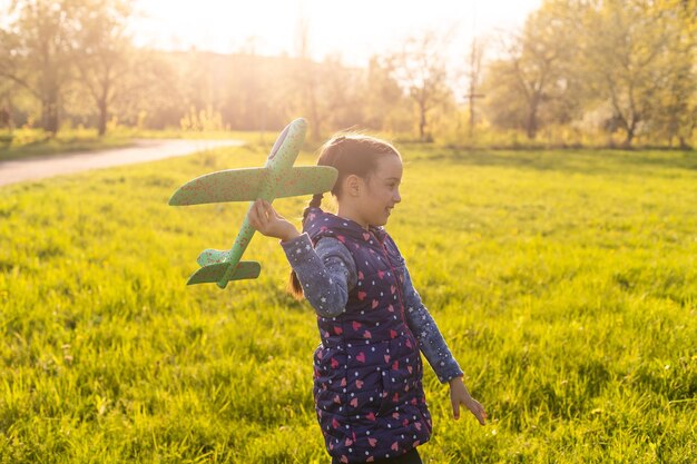 屋外の手におもちゃの飛行機を持つ少女、ゴム製モーターの風棒をねじ込みます。