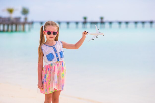 Little girl with toy airplane in hands on white sandy beach
