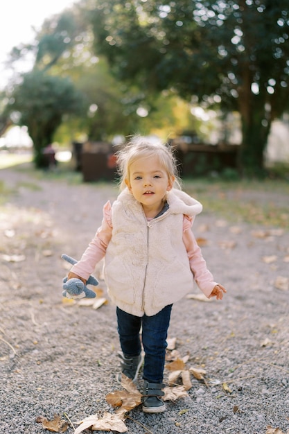 Photo little girl with a toy walks along a path among fallen leaves