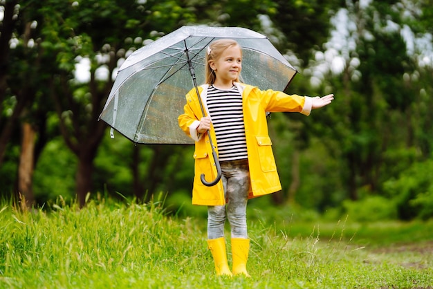 Little girl with transparent umbrella playing in the rain on\
sunny beautiful girl in a yellow cloak.
