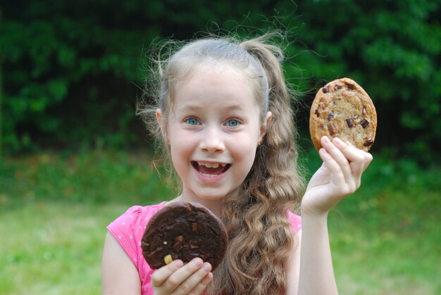  Little girl with two cookies. Unhealthy food for kids. 