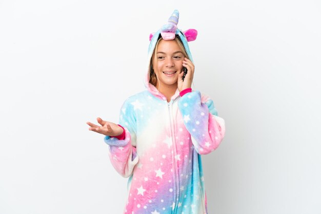 Little girl with unicorn pajamas isolated on white background keeping a conversation with the mobile phone with someone