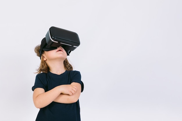 Little girl with virtual reality glasses looking up on white background