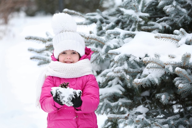 Little girl with winter clothes holding snow on hands in snowy park outdoor