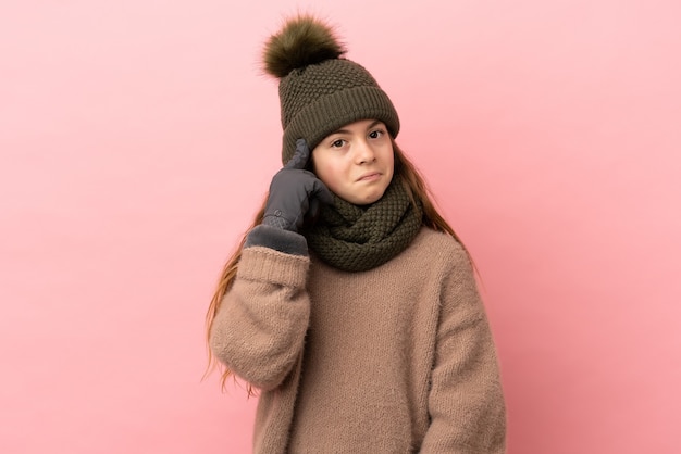 아이디어를 생각하는 분홍색 배경에 고립 된 겨울 모자와 어린 소녀