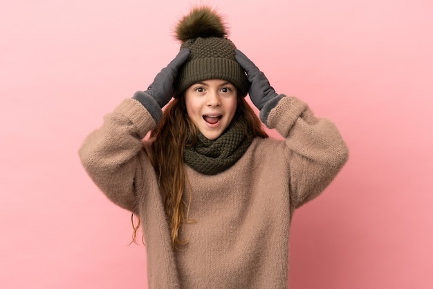 Little girl with winter hat isolated on pink background with surprise expression