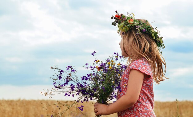 Little girl with a wreath on his head in a field of wheat