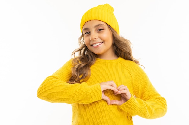 La bambina con in maglia e cappuccio gialli mostra un cuore dalle sue mani e sorrisi, ritratto isolato su bianco