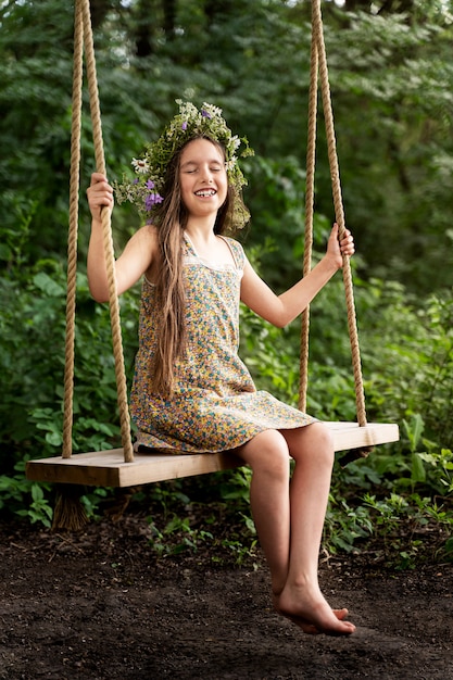 Photo little girl in a wreath of flowers rides on a swing and laughs