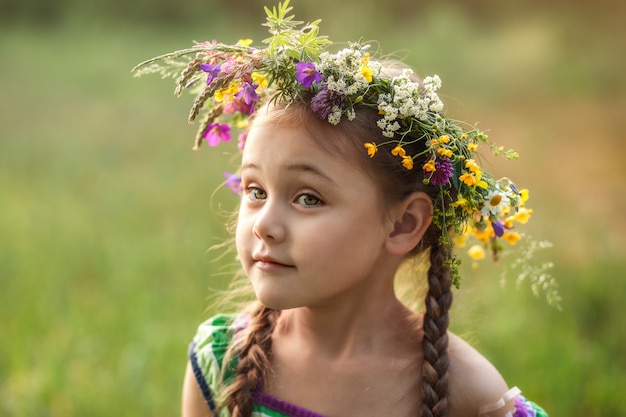 little girl in a wreath of wild flowers in summer