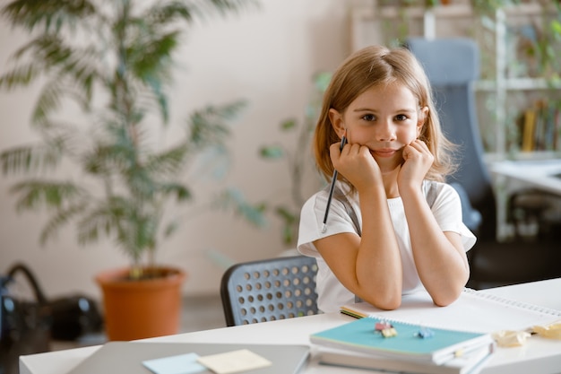 Little girl writes in notebook doing homework at desk in light room