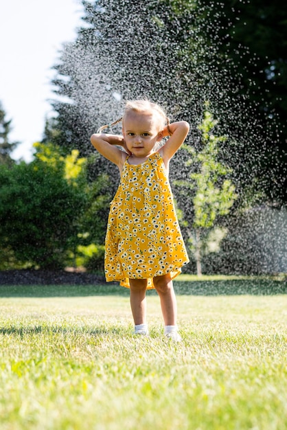 Photo a little girl in a yellow dress playing with water sprinklers.