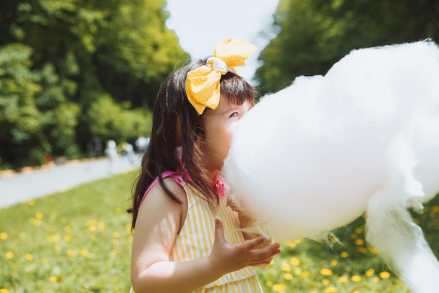 Una bambina con un vestito giallo durante una passeggiata in un parco di divertimenti mangia zucchero filato