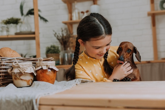 little girl in a yellow dress with a wooden spatula in her hands and jam in glass jar in the kitchen