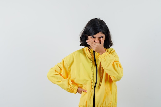 Little girl in yellow hoodie holding hand on mouth and looking mournful , front view.