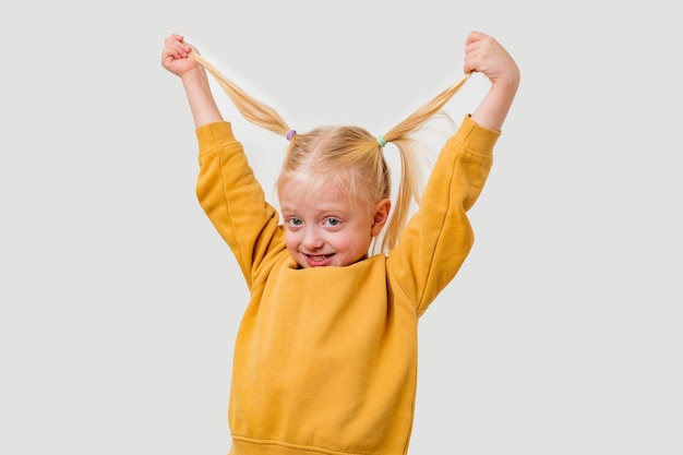 A little girl in a yellow hoodie holds her hair in the air