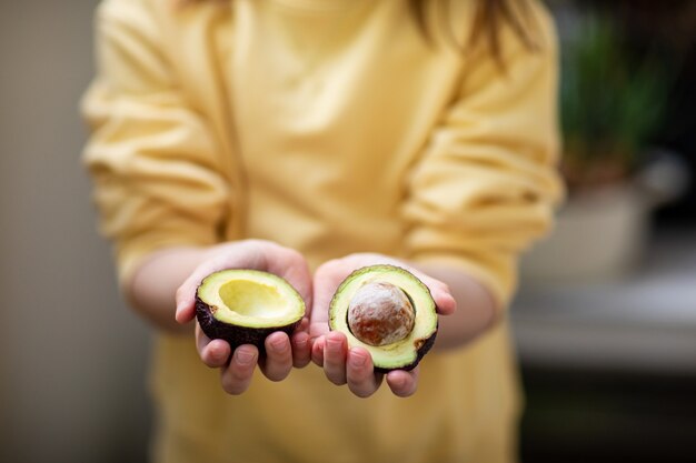 Little girl in yellow sweatshirt holding cut avocado, healthy eating concept, hands close-up