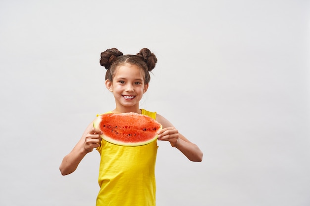 Little girl in yellow t-shirt laughing and holding slice of watermelon