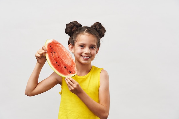 Little girl in yellow t-shirt, laughing merrily and holding slice of watermelon