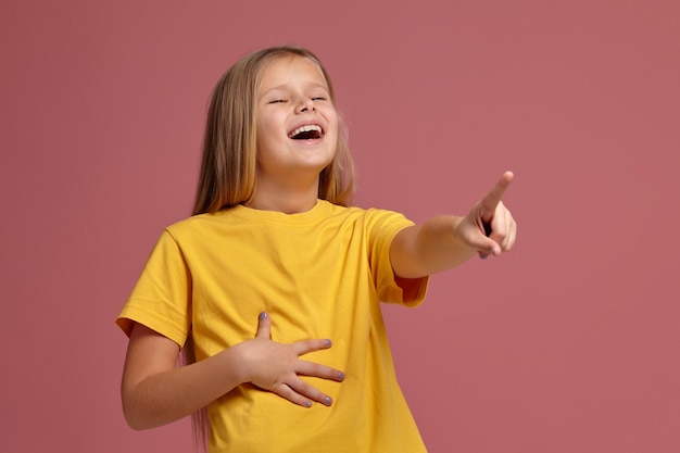 Little girl in yellow t-shirt laughs pointing finger