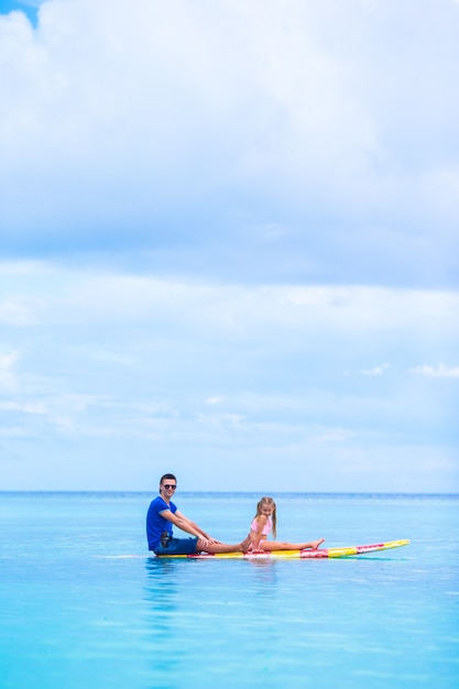 Little girl and young dad have fun on surfboard 