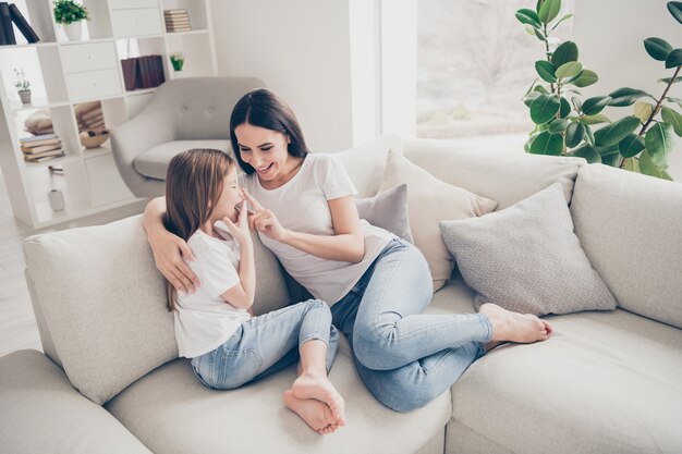 屋内の家の家で笑っているタッチ鼻を遊んで抱き締める小さな女の子の若いママ