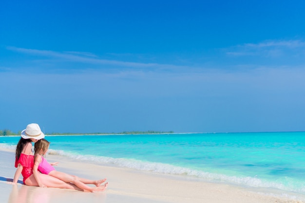 Bambina e giovane madre alla spiaggia tropicale che si siede in acque basse